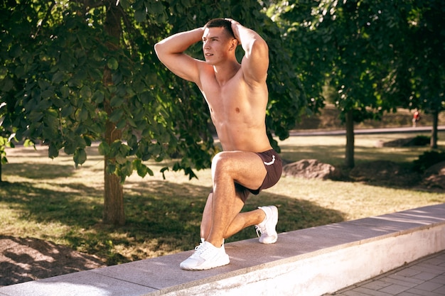 Um atleta masculino musculoso fazendo exercícios no parque. Ginástica, treino, flexibilidade de treino de fitness.