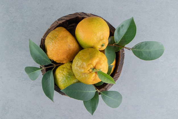 Um balde de madeira cheio de tangerinas e folhas em mármore.