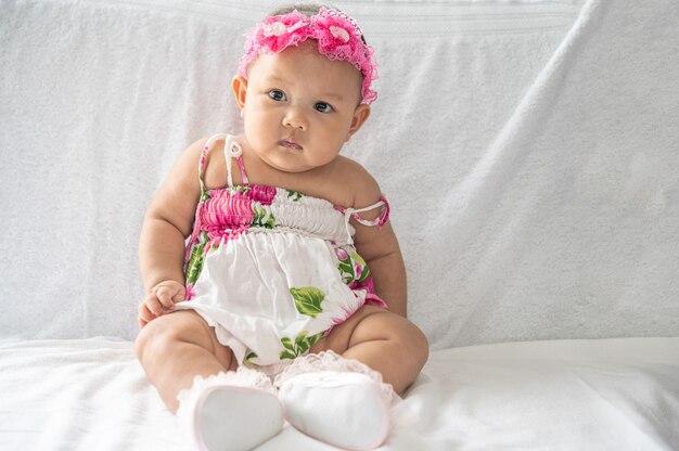 Um bebê aprende a se sentar em uma cama branca