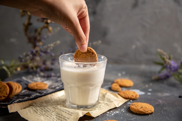 Um biscoito macho mergulhado no copo de leite com flores roxas na mesa cinza biscoito chá biscoito doce