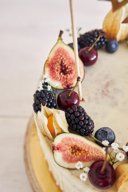 Um bolo de aniversário de frutas com cobertura de aniversário, frutas em cima e gotejamento branco sobre fundo bege