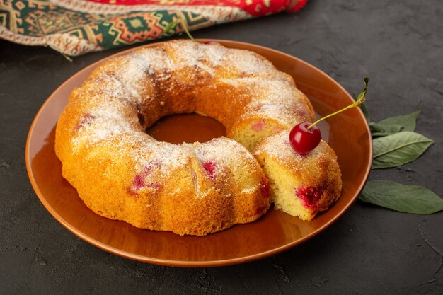 Um bolo de cereja frontal redondo formado dentro do prato na mesa escura