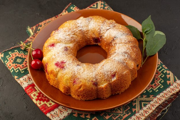 Um bolo de cereja gostoso de vista superior redondo formado dentro de um prato marrom na mesa escura bolo biscoito açúcar doce