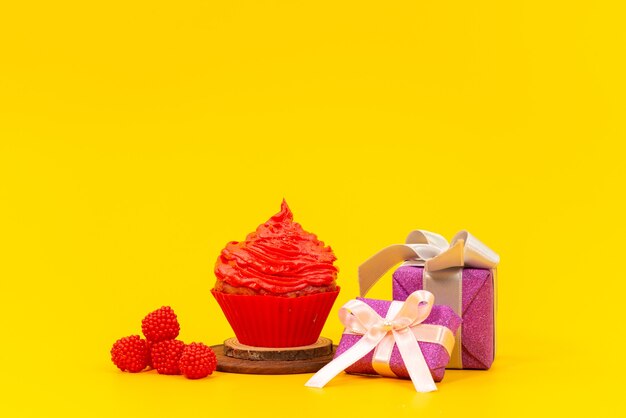 Um bolo de frutas vermelhas com framboesas vermelhas frescas e caixas de presente roxas na mesa amarela