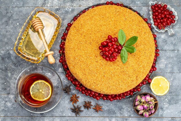 Um bolo de mel delicioso com vista de cima e assado com cranberries vermelhas na mesa cinza.