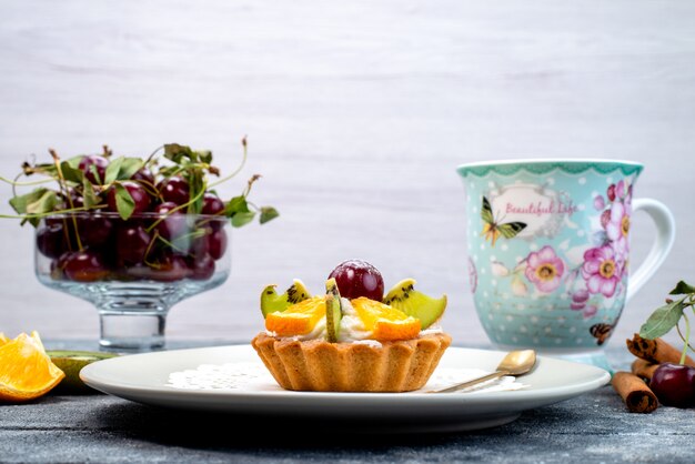 Um bolo delicioso com creme e frutas frescas fatiadas junto com chá de canela em um biscoito de mesa cinza-azulado