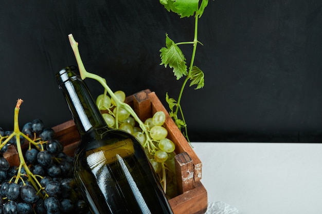 Um cacho de uvas e uma garrafa de vinho em uma mesa branca. Foto de alta qualidade