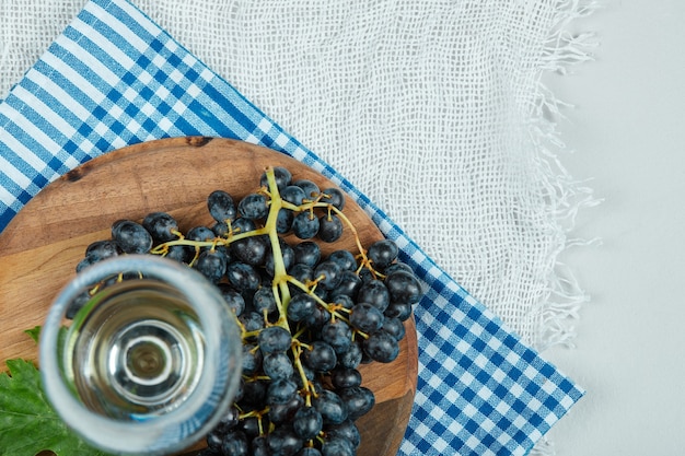 Um cacho de uvas pretas com folhas e uma taça de vinho na superfície branca