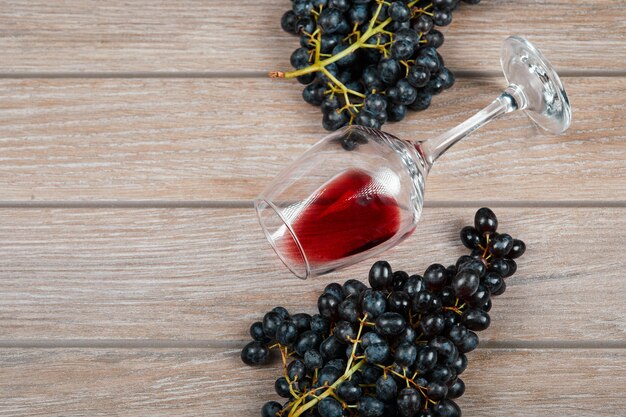 Um cacho de uvas pretas e um copo de vinho no fundo de madeira. Foto de alta qualidade