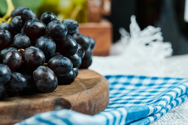 Foto grátis um cacho de uvas pretas em uma placa de madeira com uma toalha de mesa azul