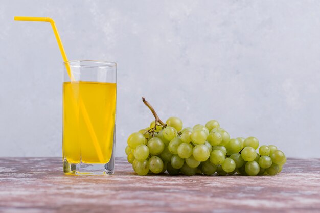 Um cacho de uvas verdes com um copo de suco na parede azul