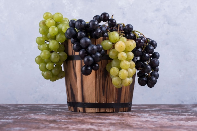 Foto grátis um cacho de uvas verdes e vermelhas em um balde de madeira