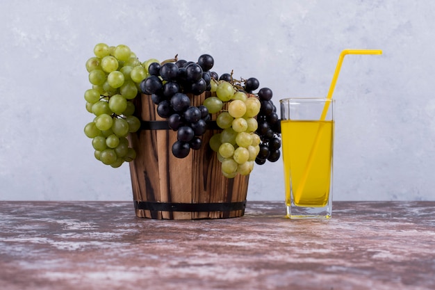 Foto grátis um cacho de uvas verdes e vermelhas em um balde e um copo de suco