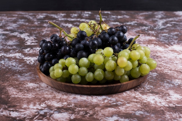 Foto grátis um cacho de uvas verdes e vermelhas em uma bandeja de madeira