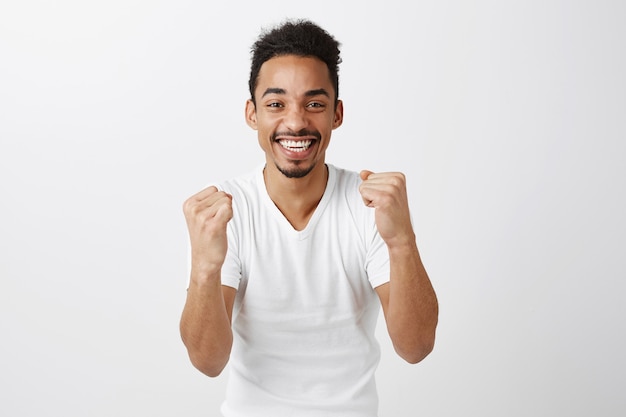 Um cara de pele escura bem-sucedido se regozijando, socando e sorrindo, dizendo sim, triunfando