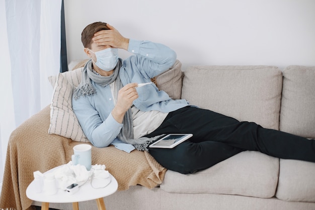 Um cara doente na sala de estar. homem de meia-idade se sentindo mal com resfriado e febre em casa. homem com uma máscara médica.