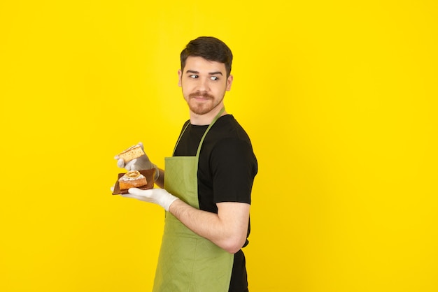 Um cara jovem e atraente segurando bolos caseiros frescos em amarelo.