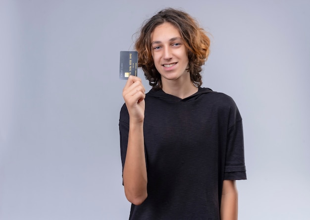 Foto grátis um cara sorridente com cabelo comprido e camiseta preta segurando um cartão na parede branca