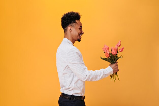 Um cara sorridente de camisa branca segurando tulipas cor de rosa