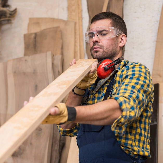 Um carpinteiro masculino olhando seriamente para prancha de madeira