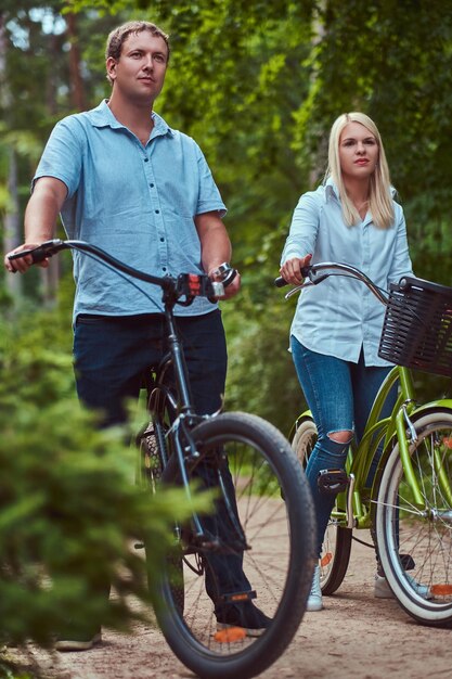 Um casal atraente de uma mulher loira e um homem vestido com roupas casuais em um passeio de bicicleta em um parque.