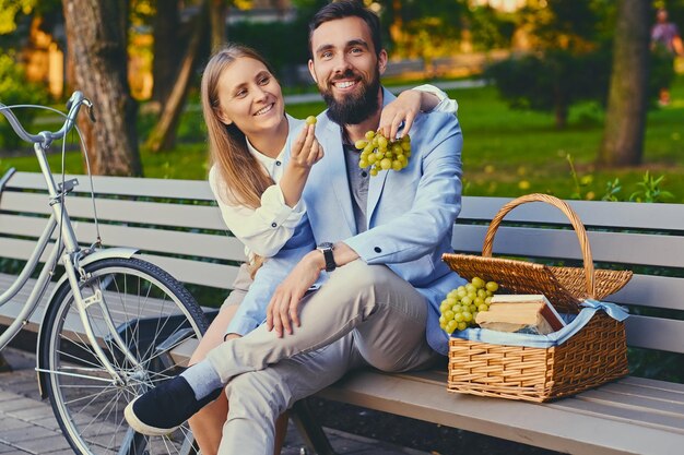 Um casal come uva em um banco em um parque.