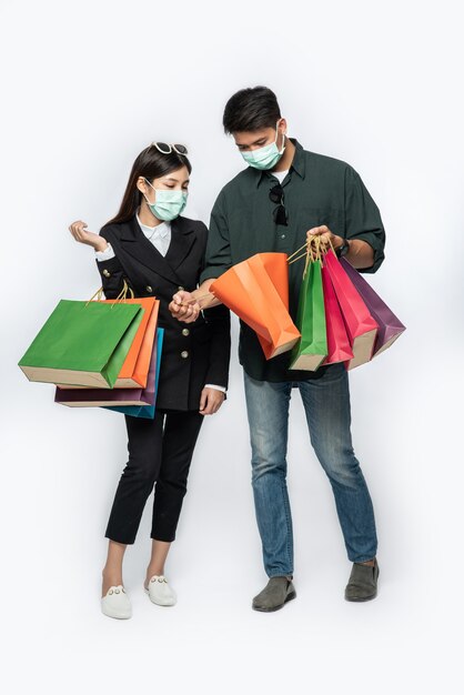Um casal de homens e mulheres usando máscaras e carregando muitos sacos de papel para fazer compras