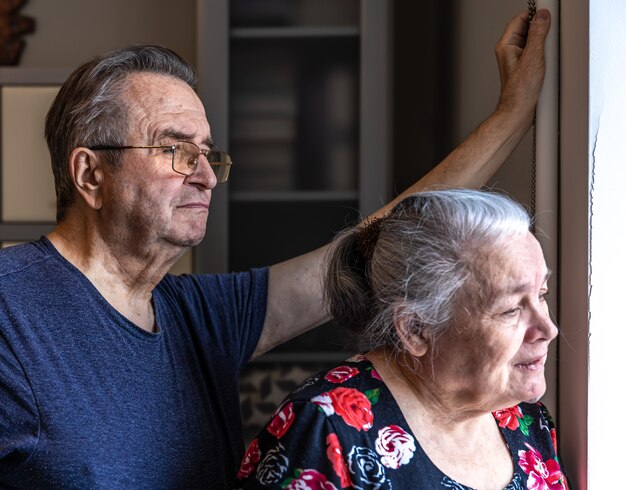 Um casal de idosos está de pé na janela e olha para alguém.