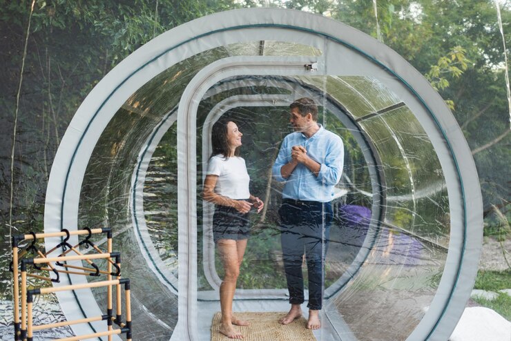 Foto grátis um casal entrando dentro de uma tenda de bolha transparente em uma floresta exuberante e natureza ao redor