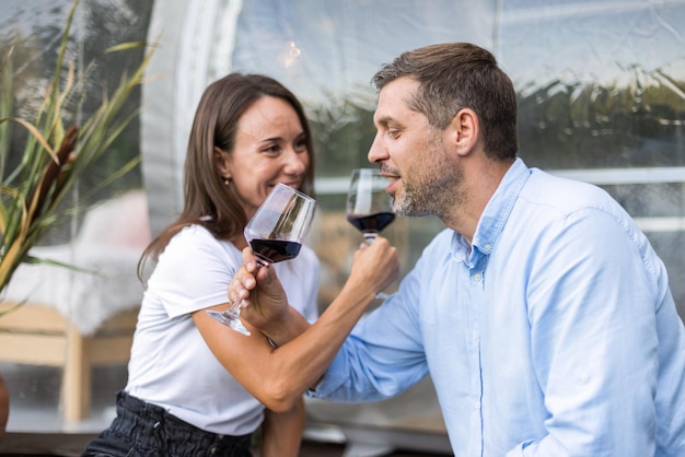 Um casal feliz bebendo vinho perto de uma tenda de bolhas transparentes em glamping