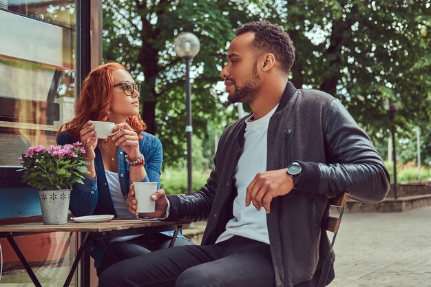 Um casal namorando tomando café, sentado perto da cafeteria. Ao ar livre em um encontro.