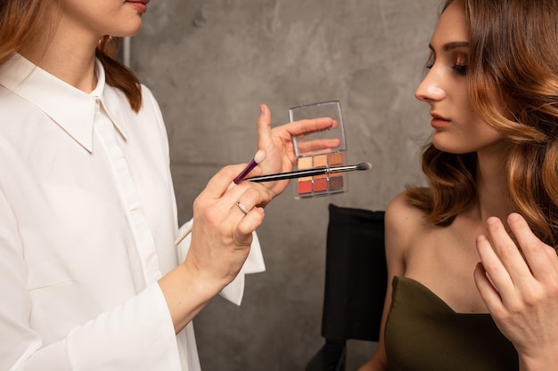 Um close-up de um maquiador segurando uma paleta com sombras para a namorada de uma modelo em um fundo cinza com um lugar para texto. tendências de maquiagem