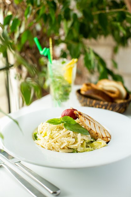Um close-up vista frontal refeição saborosa macarrão cozido com folhas verdes e carne dentro de chapa branca na mesa branca