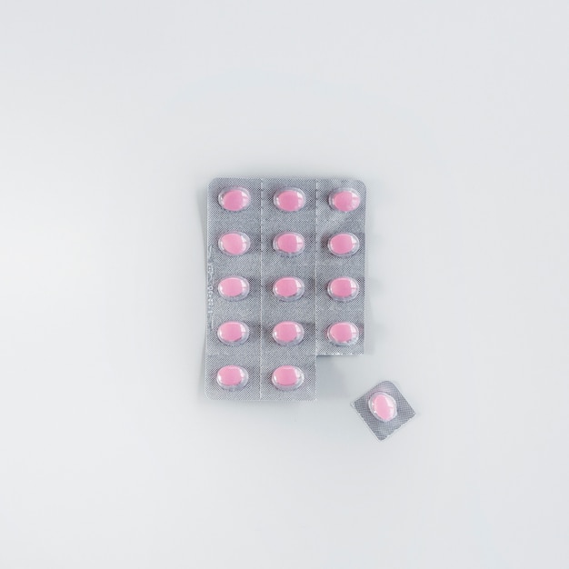 Um comprimido rosa cortado da bolha sobre o fundo branco