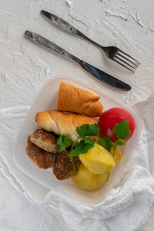 Um conceito de hora do almoço, comendo do recipiente de plástico com carne e batatas nas mesas