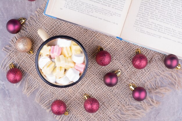 Um copo de bebida com marshmallows e bolas vermelhas de natal ao redor