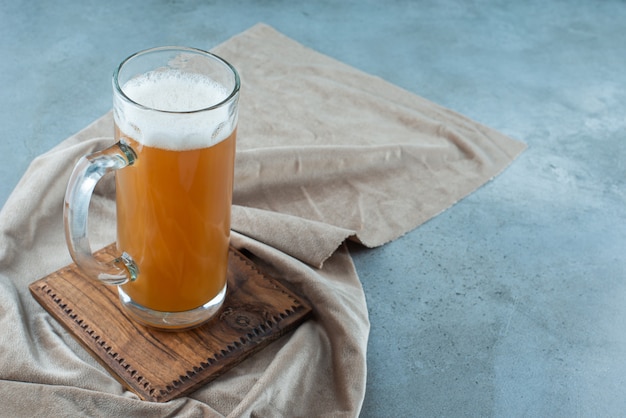 Um copo de cerveja em uma placa sobre uma toalha, sobre o fundo azul.