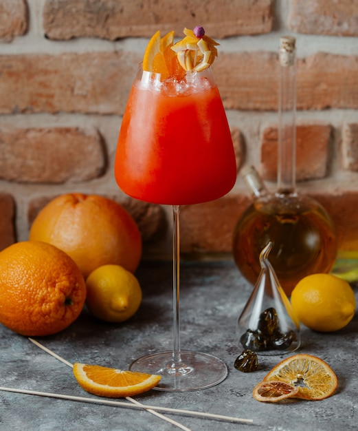 Um copo de cocktail vermelho alaranjado com fatias de laranja na parte superior.