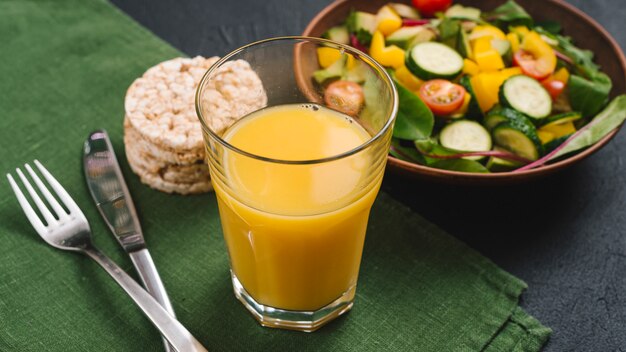 Um copo de suco; bolo de arroz tufado e salada vegan no guardanapo verde com talheres