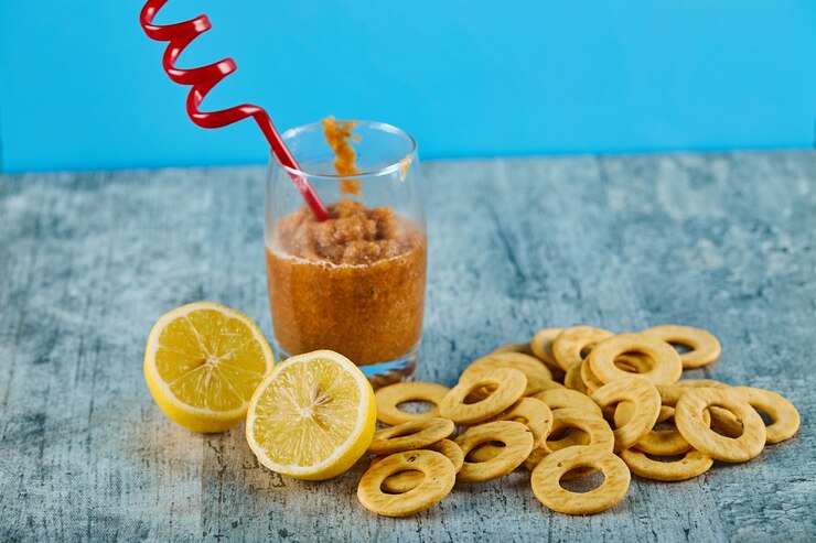 Foto grátis um copo de suco com palha, limões e biscoitos na mesa cinza.