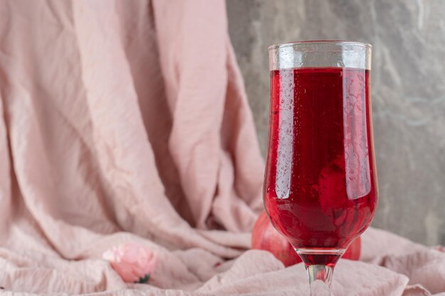 Um copo de suco com romã fresca em um pano rosa