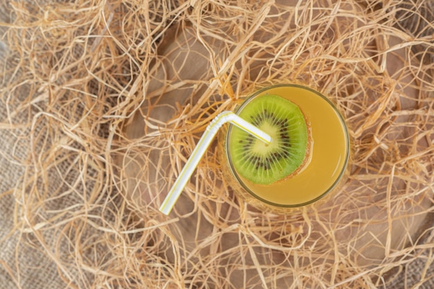 Um copo de suco com uma fatia de kiwi e canudo na serapilheira