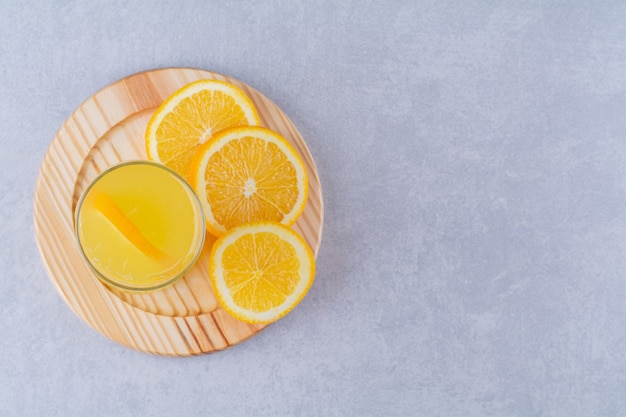 Um copo de suco de laranja ao lado de uma fatia de laranja em uma placa de madeira, no fundo de mármore.