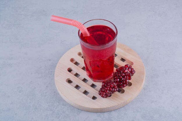 Um copo de suco de romã na peça de madeira com canudo. Foto de alta qualidade