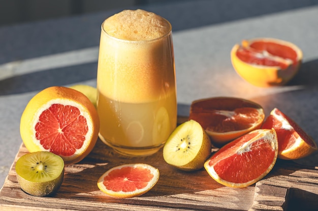 Foto grátis um copo de suco e frutas recém-espremidos em uma tábua de corte de madeira