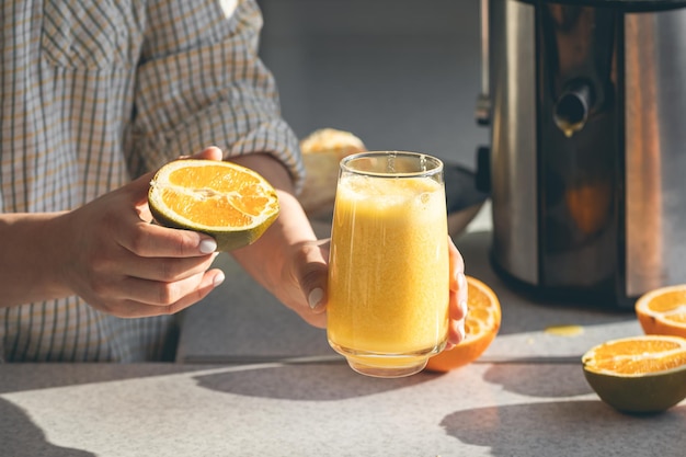Um copo de sumo de laranja recém-espremido e meia laranja nas mãos femininas.