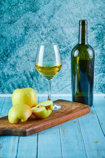 Foto grátis um copo de vinho branco e uma garrafa com fatias de maçã na parede azul.