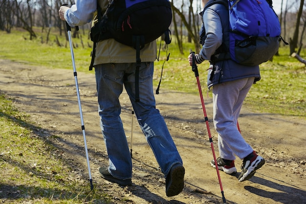 Um coração para dois andarilhos. Casal idoso da família de homem e mulher em roupa de turista, caminhando no gramado verde perto de árvores em dia ensolarado. Conceito de turismo, estilo de vida saudável, relaxamento e união.