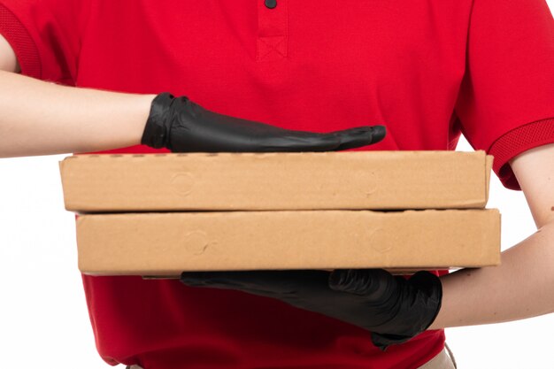 Um correio feminino vista frontal em luvas de camisa vermelha preta segurando caixas de pizza