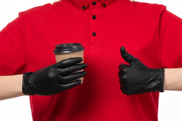 Um correio feminino vista frontal na camisa vermelha e luvas pretas, mostrando como sinal segurando a xícara de café